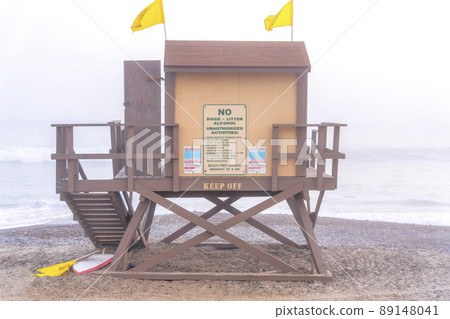 Wooden lifeguard tower with two yellow flags on top against the foggy beach of San Clemente, CA 89148041