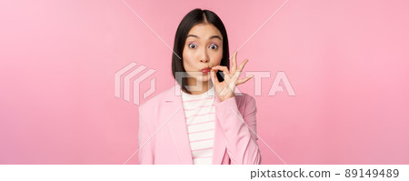 Portrait of asian corporate woman showing mouth seal, close shut lips on key gesture, promise keep secret, standing over pink background in suit Portrait of asian corporate woman showing mouth seal, close shut lips on key gesture, promise keep secret, standing over pink background in suit 89149489