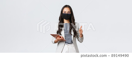 Business, finance and employment, covid-19 preventing virus and social distancing concept. Smiling real estate broker wearing protective mask during meeting, pointing camera, hold digital tablet Business, finance and employment, covid-19 preventing virus and social distancing concept. Smiling real estate broker wearing protective mask during meeting, pointing camera, hold digital tablet 89149490