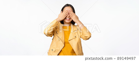 Beautiful, happy asian woman shuts eyes, blindfolded waiting for surprise and smiling, anticipating gifts on holiday, standing over white background Beautiful, happy asian woman shuts eyes, blindfolded waiting for surprise and smiling, anticipating gifts on holiday, standing over white background 89149497