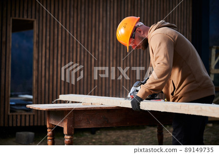 Carpenter using circular saw for cutting wooden truss. Man worker building wooden frame house. Carpentry concept. Carpenter using circular saw for cutting wooden truss. Man worker building wooden frame house. Carpentry concept. 89149735