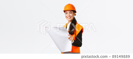 Pleased smiling female asian construction manager following blueprints during building house, looking satisfied at camera, studying architect plan, standing white background in safety helmet Pleased smiling female asian construction manager following blueprints during building house, looking satisfied at camera, studying architect plan, standing white background in safety helmet 89149889
