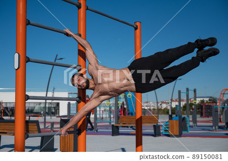 Shirtless man doing human flag outdoors.  89150081