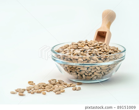 Glass bowl filled with peeled sunflower seeds with a small wooden spoon isolated in the white background. Close-up Glass bowl filled with peeled sunflower seeds with a small wooden spoon isolated in the white background. Close-up 89151009