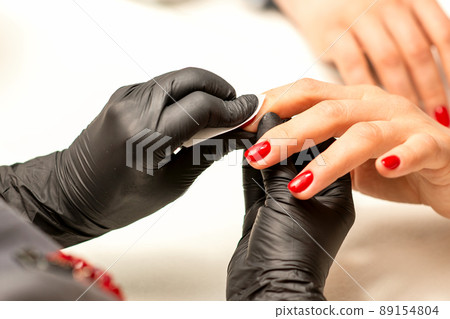 The manicurist finishes the procedure for red nail polishing and cleaning with a cotton napkin, pad, swab in a beauty salon, close up The manicurist finishes the procedure for red nail polishing and cleaning with a cotton napkin, pad, swab in a beauty salon, close up 89154804