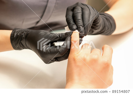 The manicurist finishes the procedure for red nail polishing and cleaning with a cotton napkin, pad, swab in a beauty salon, close up The manicurist finishes the procedure for red nail polishing and cleaning with a cotton napkin, pad, swab in a beauty salon, close up 89154807