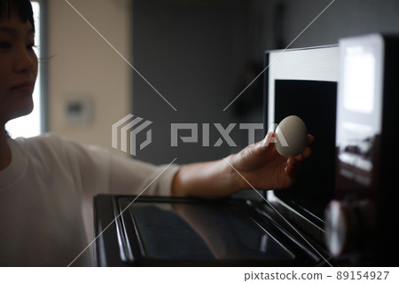 A woman trying to heat an egg in the microwave 89154927