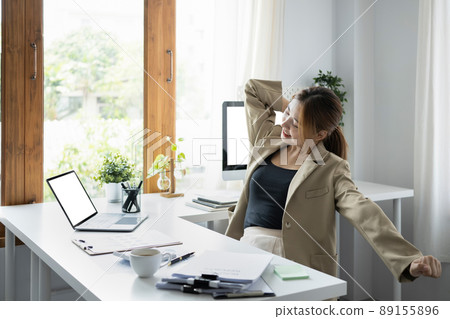 Young female employee stretching arms, relaxing from work in office. Young female employee stretching arms, relaxing from work in office. 89155896