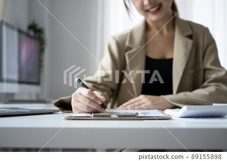 Cropped shot smiling female finance manager planning work projects at office desk. Cropped shot smiling female finance manager planning work projects at office desk. 89155898