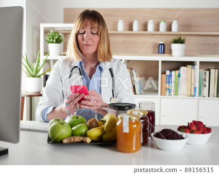 distracted female nutritionist chatting with smartphone in office studio 89156515