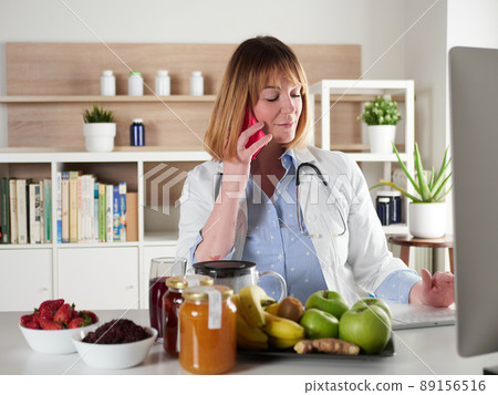 distracted female nutritionist chatting with smartphone in office studio 89156516