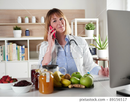 distracted female nutritionist chatting with smartphone in office studio 89156517