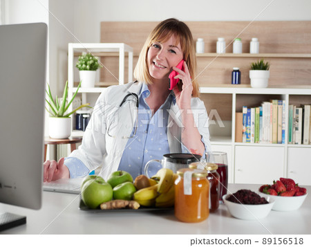 distracted female nutritionist chatting with smartphone in office studio 89156518
