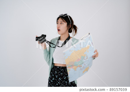 Portrait of smiling young female Asian tourist backpacker holding map and camera in isolated white background - summer travel concept 89157039