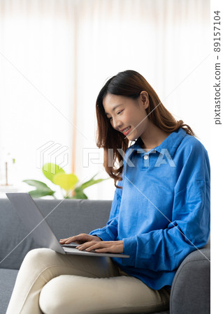 Young asian business woman smile and work from home with laptop computer online to internet on sofa in living room, freelance girl using notebook on couch with comfort, new normal, lifestyle concept 89157104