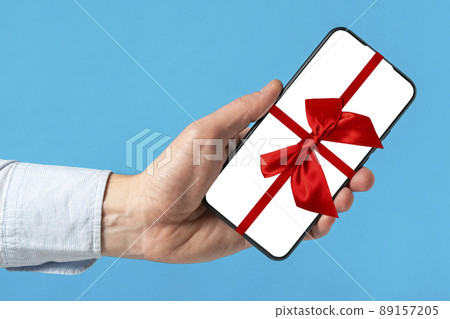 Smartphone in a man's hand tied with a red ribbon and a bow Smartphone in a man's hand tied with a red ribbon and a bow 89157205