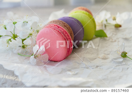 cakes macaroons of red, brown purple, green and beige on white paper with apple blossoms cakes macaroons of red, brown purple, green and beige on white paper with apple blossoms 89157460