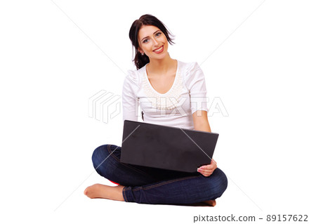 A female student sits on the floor with her legs crossed and does her homework on a laptop A female student sits on the floor with her legs crossed and does her homework on a laptop 89157622