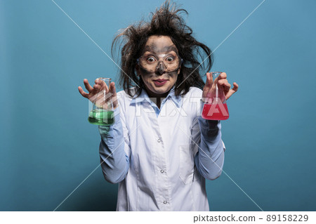 Crazy chemist holding glass flasks filled with toxic chemical compounds after laboratory explosion. Mad wacky lab worker having beakers filled with liquid substances after failed laboratory experiment Crazy chemist holding glass flasks filled with toxic chemical compounds after laboratory explosion. Mad wacky lab worker having beakers filled with liquid substances after failed laboratory experiment 89158229