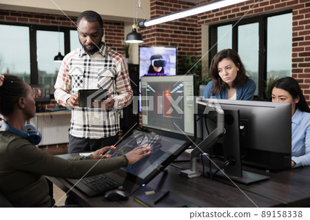 Game industry developer with multiple displays on desk working on level design and environment. Production department employees in office workspace developing videogame technology. 89158338