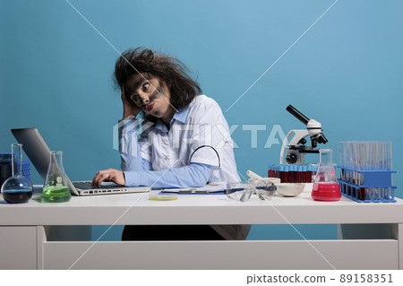 Wild foolish woman with dirty face researching discovery on laptop after chemistry laboratory explosion. Crazy silly scientist acting funny and confused after analyzing experiment anomalies report. 89158351