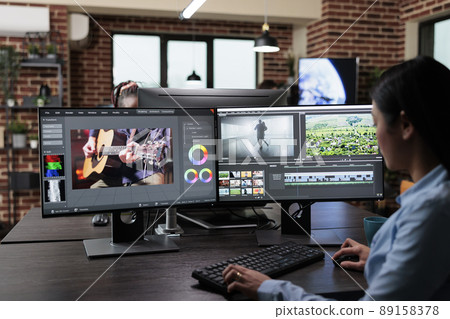 Creative company professional movie footage editor sitting at multi monitor workstation while editing film frames. Expert videographer improving video quality using specialized software. Creative company professional movie footage editor sitting at multi monitor workstation while editing film frames. Expert videographer improving video quality using specialized software. 89158378