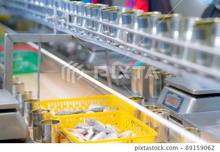 Canned fish factory. Food industry. Sardines in yellow plastic basket waiting for worker to fill in tinned cans. Food processing production line. Food manufacturing industry. Many can on conveyor belt 89159062
