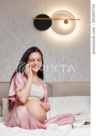 Pregnant woman sitting on bed and using smartphone 89160759