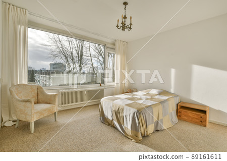 The interior of a bright bedroom with a checkered bed, an armchair next to it and a carpet floor The interior of a bright bedroom with a checkered bed, an armchair next to it and a carpet floor 89161611