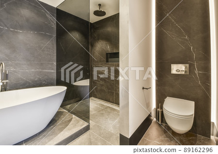 The interior of a marble bathroom with a ceramic bathtub and a hinged toilet in a cozy house The interior of a marble bathroom with a ceramic bathtub and a hinged toilet in a cozy house 89162296