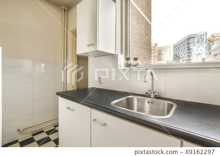 A small kitchen with lots of cabinets and a metal sink on the tiled floor A small kitchen with lots of cabinets and a metal sink on the tiled floor 89162297