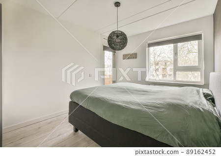 A small bedroom in white tones with a large bed and a window overlooking the street A small bedroom in white tones with a large bed and a window overlooking the street 89162452