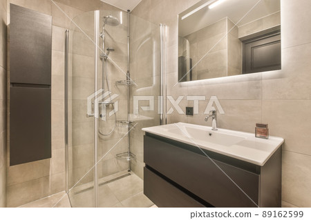The interior of the bathroom with a sink built into the cabinet under the mirror and a shower cabin surrounded by tiles 89162599