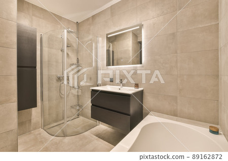 The interior of the bathroom with a sink built into the cabinet under the mirror bathtub and a shower cabin surrounded by tiles 89162872