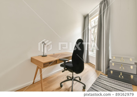 A small work area with a wooden table and an ergonomic chair next to the window 89162979