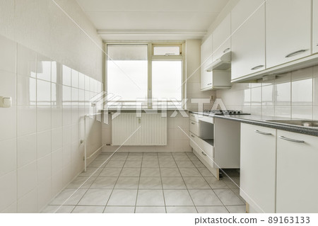 Kitchen with white furniture and tiled floor in the apartment of a residential building Kitchen with white furniture and tiled floor in the apartment of a residential building 89163133