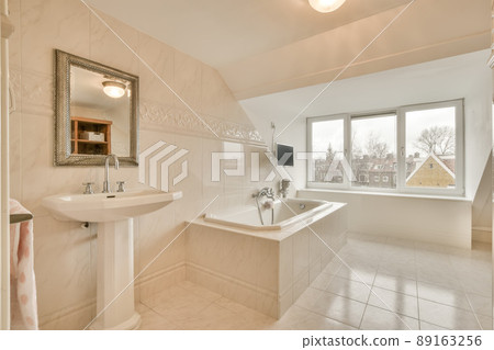 Spacious bathroom with white tiles, sink, bathtub next ot the window Spacious bathroom with white tiles, sink, bathtub next ot the window 89163256