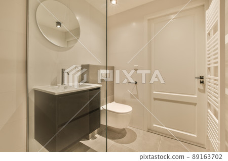 The interior of the bathroom with a toilet and a ceramic sink under a round mirror 89163702
