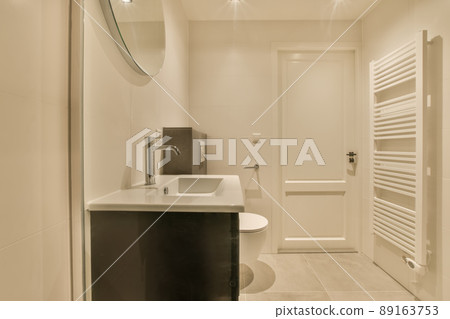 The interior of the bathroom with a toilet and a ceramic sink under a round mirror The interior of the bathroom with a toilet and a ceramic sink under a round mirror 89163753