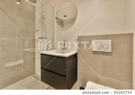 The interior of the bathroom with a shower stall and a ceramic sink under a round mirror The interior of the bathroom with a shower stall and a ceramic sink under a round mirror 89163754