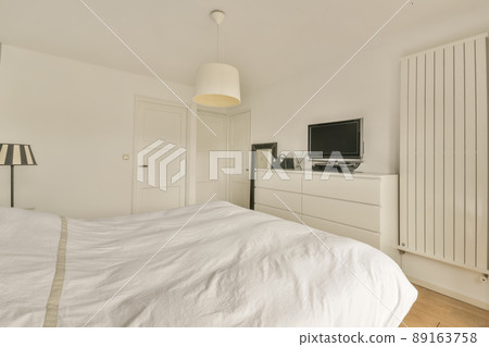 A small bedroom with a TV in front of a white bed in a cozy modern house A small bedroom with a TV in front of a white bed in a cozy modern house 89163758
