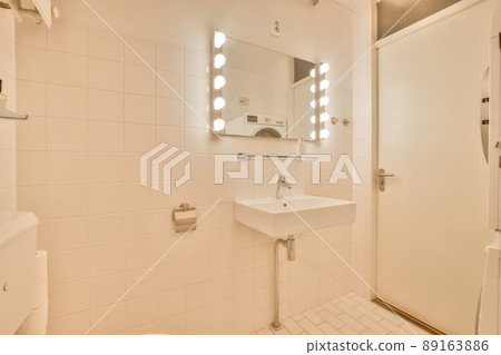 The interior of a bathroom decorated with white tiles with a ceramic sink and a mirror with lighting in a modern house The interior of a bathroom decorated with white tiles with a ceramic sink and a mirror with lighting in a modern house 89163886