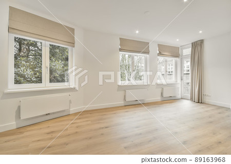 A large room in an empty new house with large windows in a minimalist style, made in white tones A large room in an empty new house with large windows in a minimalist style, made in white tones 89163968