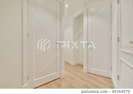 Interior of long narrow hallway with closed door, wooden floor and white walls in apartment designed in minimal style. 89164079