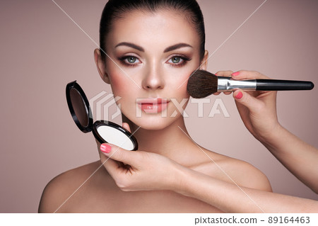 Beautiful woman applies skin tone with brush 89164463
