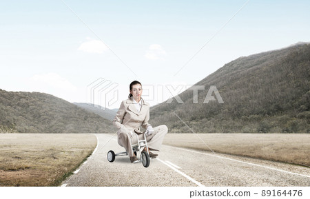 Caucasian woman riding kid's bicycle on road 89164476