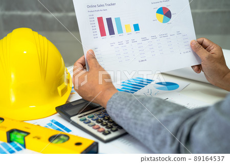 Asian engineer with architectural house plan project blueprint, graph and yellow helmet and engineering construction tools. 89164537