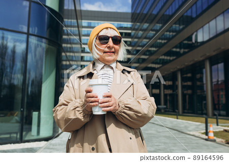 Portrait of Successful Business Woman in yellow hat and sunglasses holding cup of hot drink in hand. Attractive businesswoman drinking a coffee in paper bio white cup. Business on the go concept. Portrait of Successful Business Woman in yellow hat and sunglasses holding cup of hot drink in hand. Attractive businesswoman drinking a coffee in paper bio white cup. Business on the go concept. 89164596