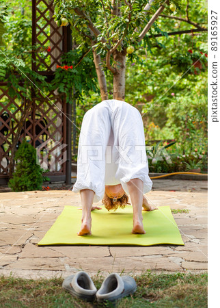 Young woman practices yoga in the garden. Downward Dog Pose - Downward-facing Dog Pose, also called Adho Mukha Shvanasana 89165927