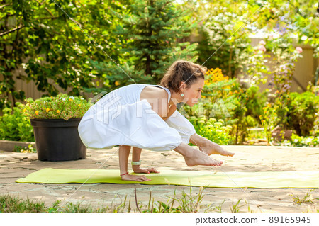 Young woman practices yoga in the courtyard of a country house. Titibhasana 89165945